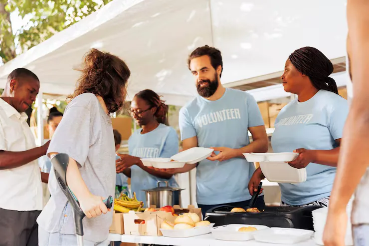Volunteers in matching shirts serving meals to guests under an outdoor tent
