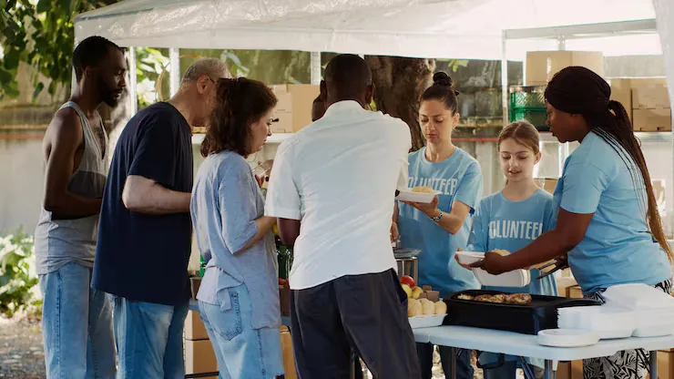 A volunteer team, including a young girl, handing out food at an outdoor serving line
